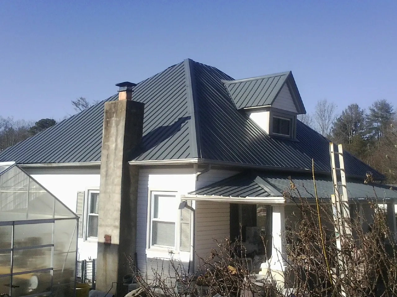 Dark blue standing seam metal roof on a white farmhouse with dormer — Slate & Tile Roof Repair by Roofing Brothers in Balko