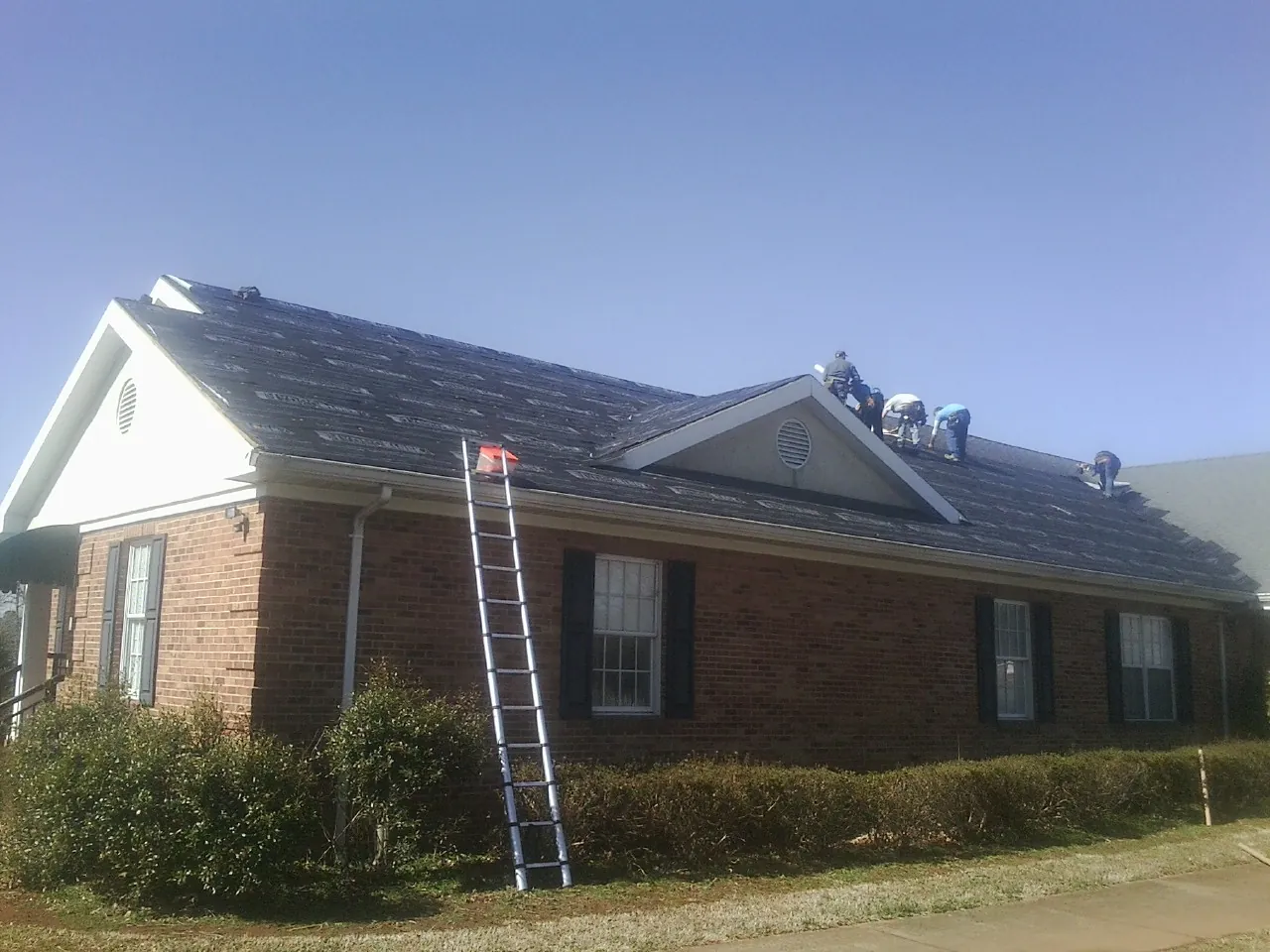 Crew tearing shingles off a brick ranch roof with a ladder set — Emergency Roof Repair work by our crew in Balko