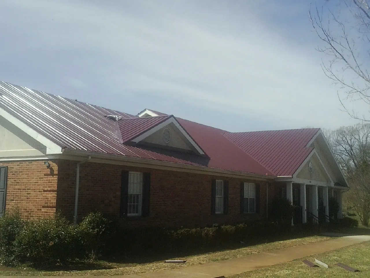 Red metal roof with gabled entries on a long brick building, from a Hail Damage Roof Repair job in Balko