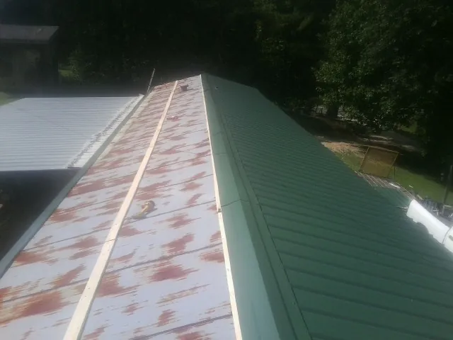 Old rusted panels beside newly installed green metal roofing — Wind Damage Roof Repair by Roofing Brothers in Balko