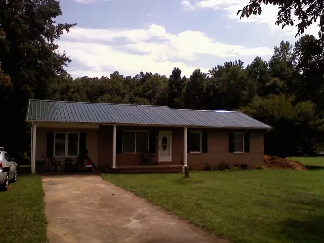 Dark green metal roof on a brick ranch with a covered porch in Balko
