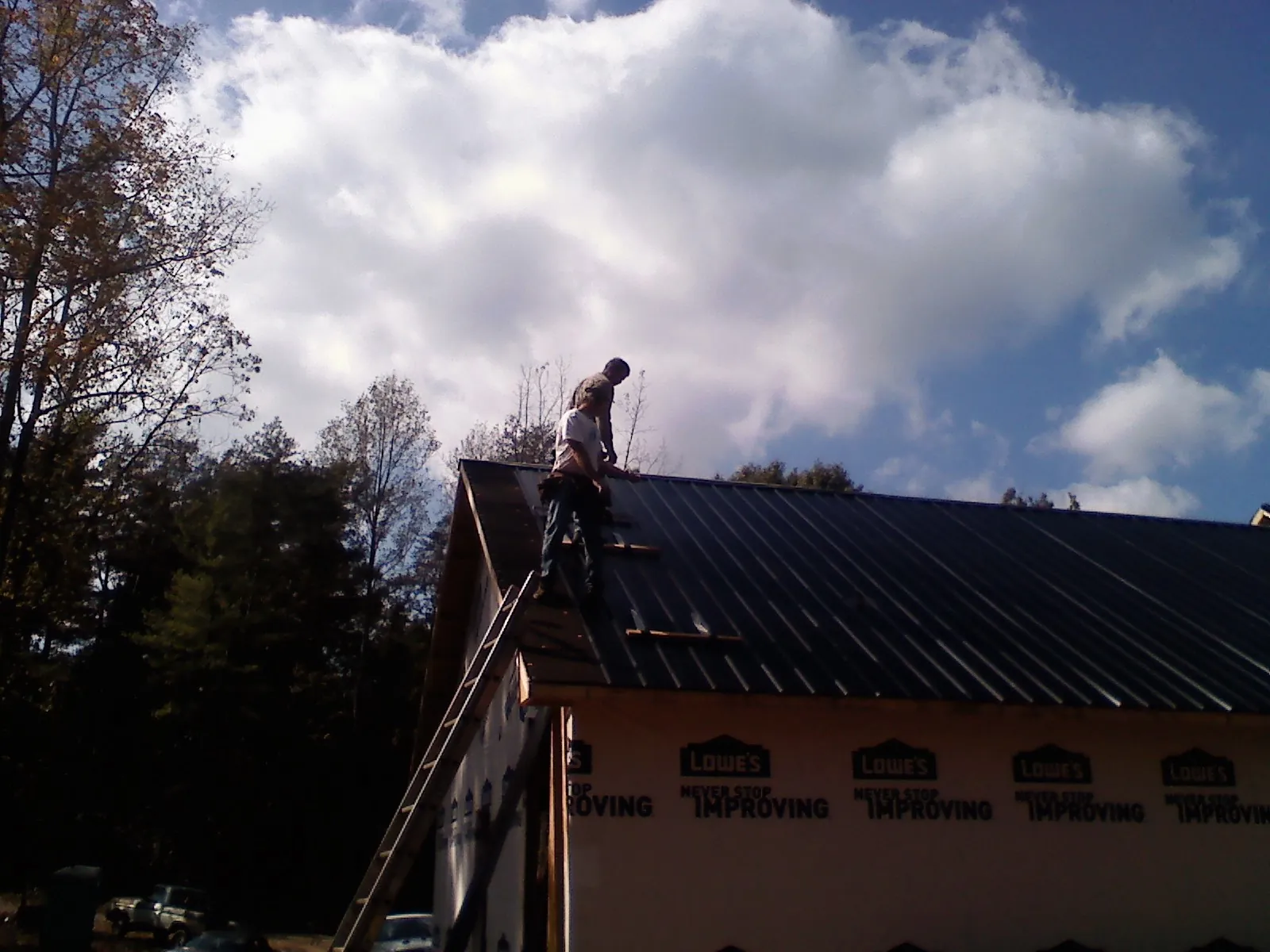 Roofer fastening dark metal panels high against a cloudy sky, from a Roof Inspection job in Balko