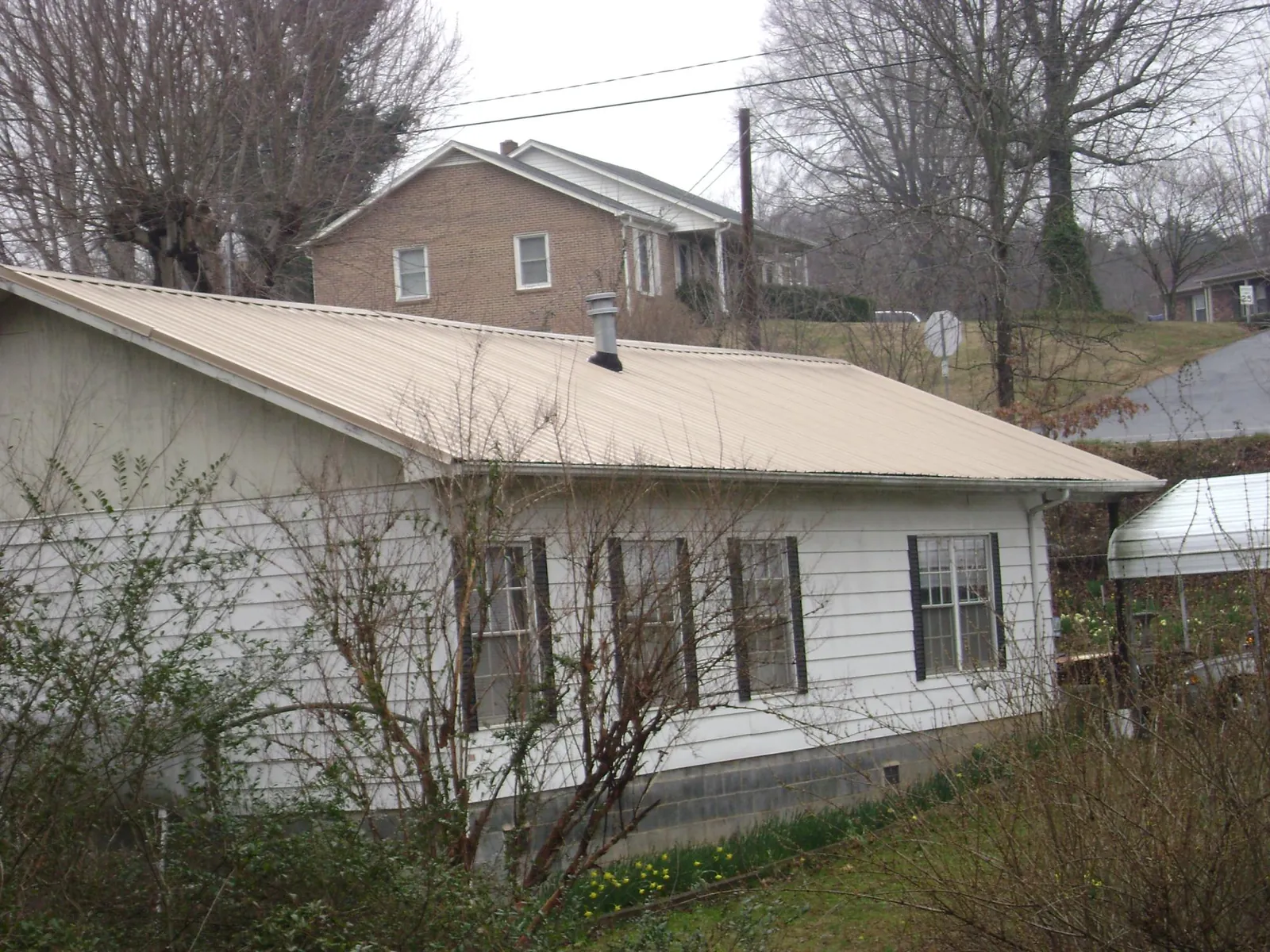 Tan metal roof on a white sided house set into a hillside — Commercial Roofing by Roofing Brothers in Balko