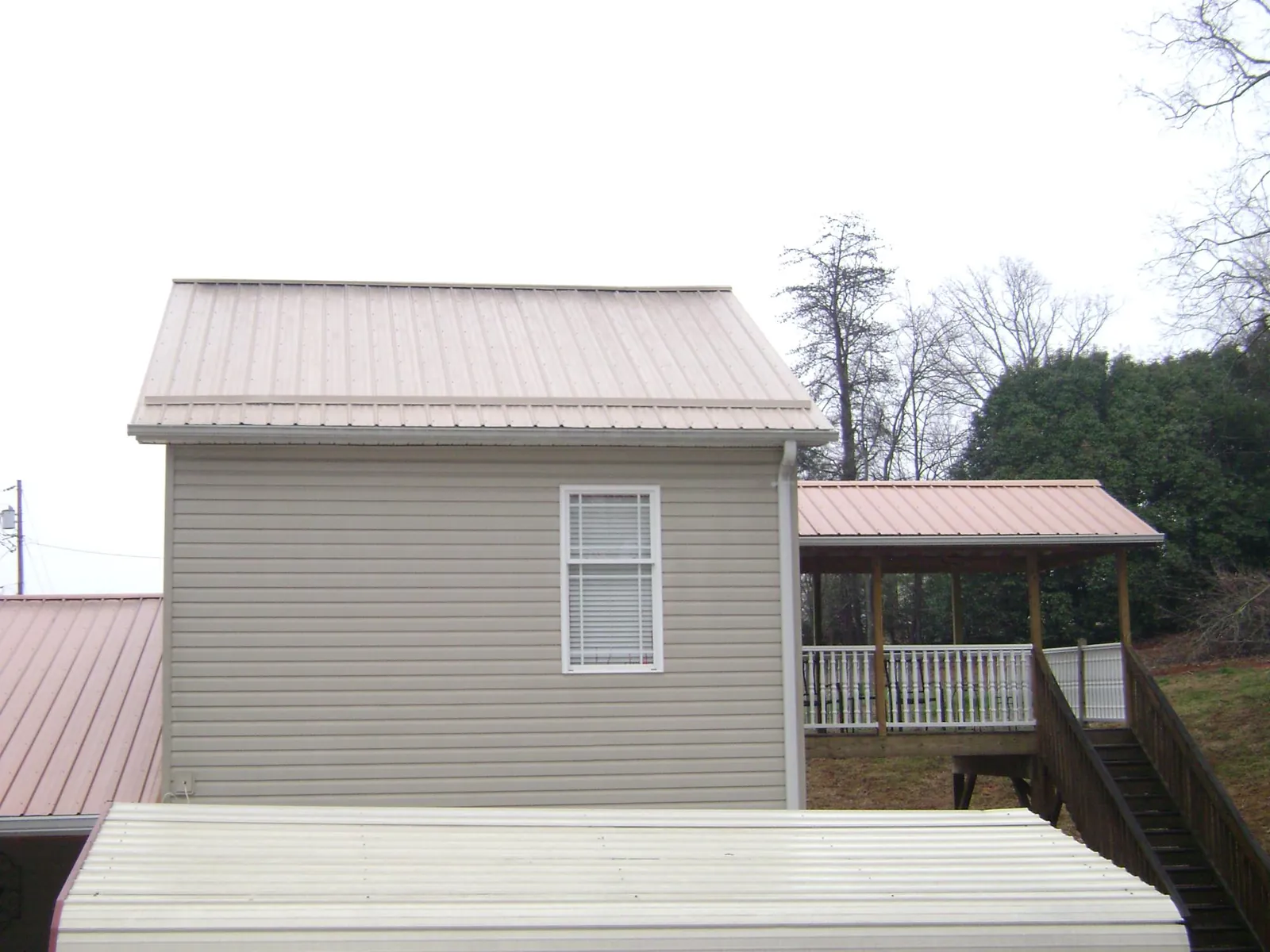 Tan metal roofs on a two story addition and attached porch, from a Roof Replacement job in Balko